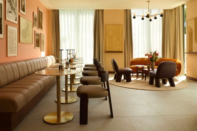 Salle lumineuse avec banquettes en cuir, tables dorées, chaises modernes et coin salon avec fauteuils et canapé.