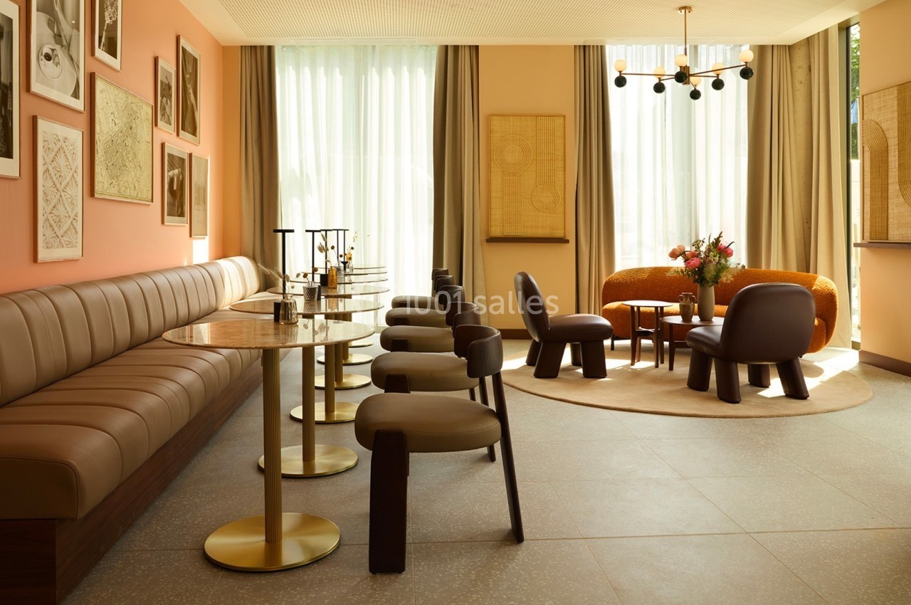 Salle lumineuse avec banquettes en cuir, tables dorées, chaises modernes et coin salon avec fauteuils et canapé.