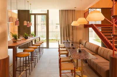Salle lumineuse avec banquettes en cuir, tables dorées, chaises modernes et coin salon avec fauteuils et canapé.