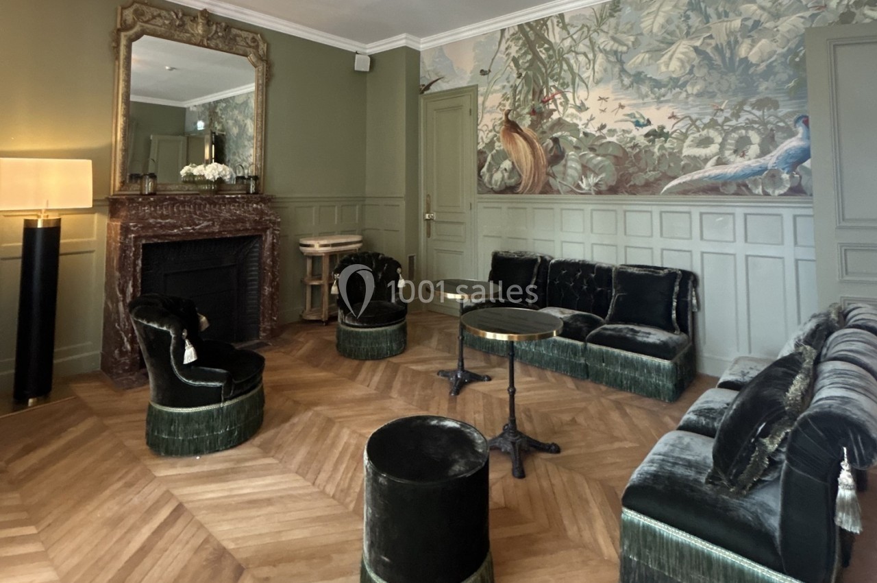 Salon élégant avec mobilier en velours vert, cheminée ornée d'un miroir, parquet en chevrons et fresque murale exotique.