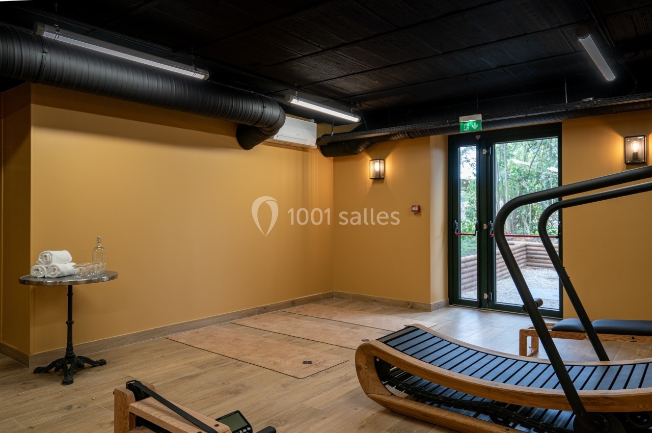 Salle de sport avec équipement en bois, murs orange, sol en bois, table avec serviettes et porte vitrée donnant sur l…