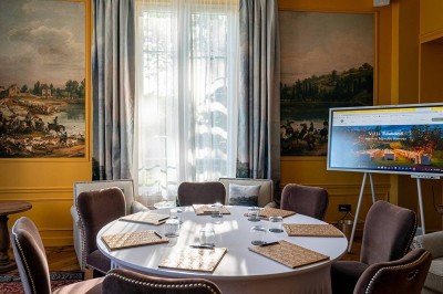 Salle de réunion lumineuse avec table en bois, chaises rembourrées, bouteilles d'eau et grandes fenêtres avec rideaux…
