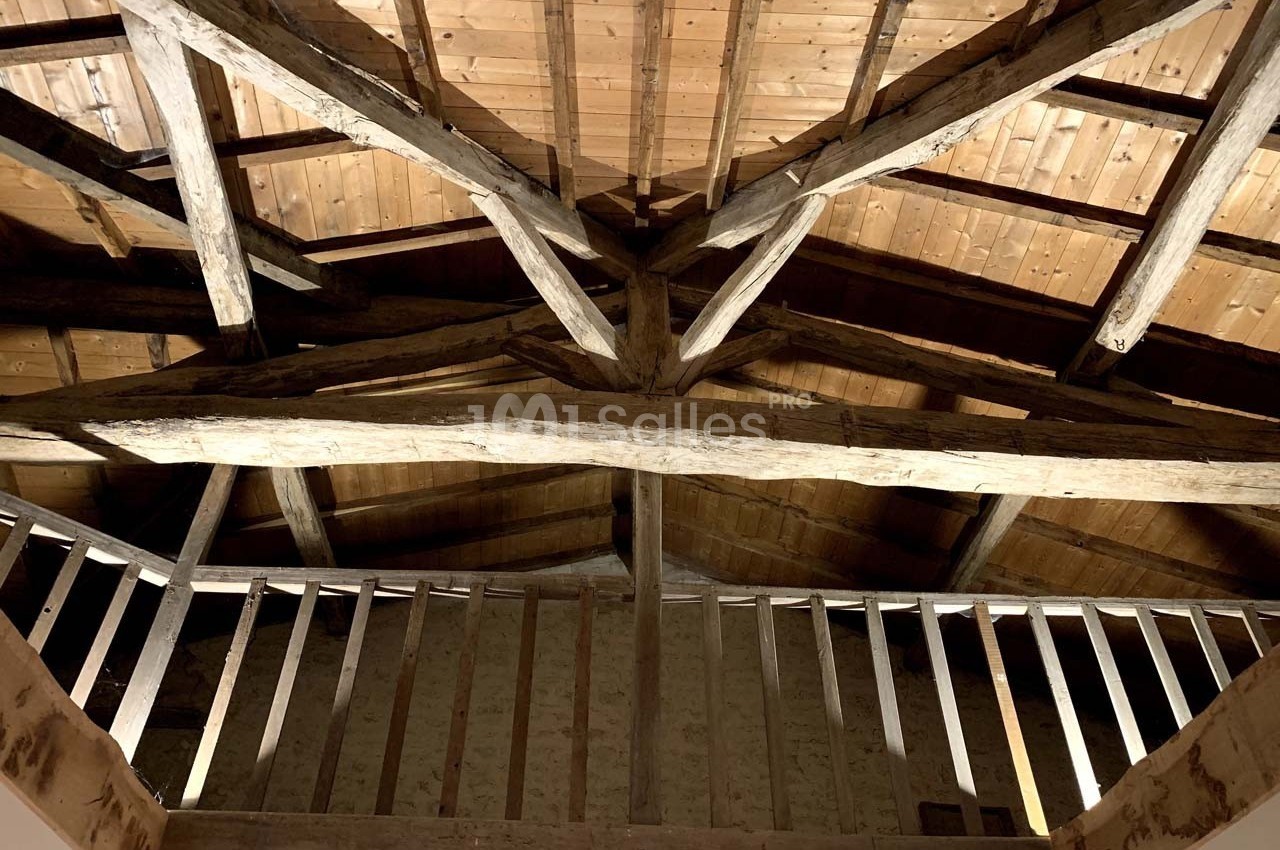Charpente en bois apparente d'un plafond incliné, vue depuis un escalier avec une rambarde en bois.