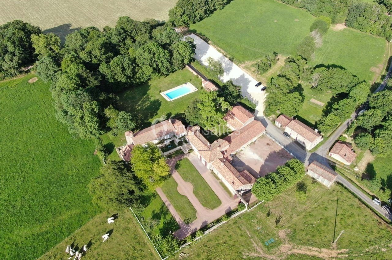 Vue aérienne d'un domaine rural avec bâtiments en briques, piscine, espaces verts et pâturages environnants.