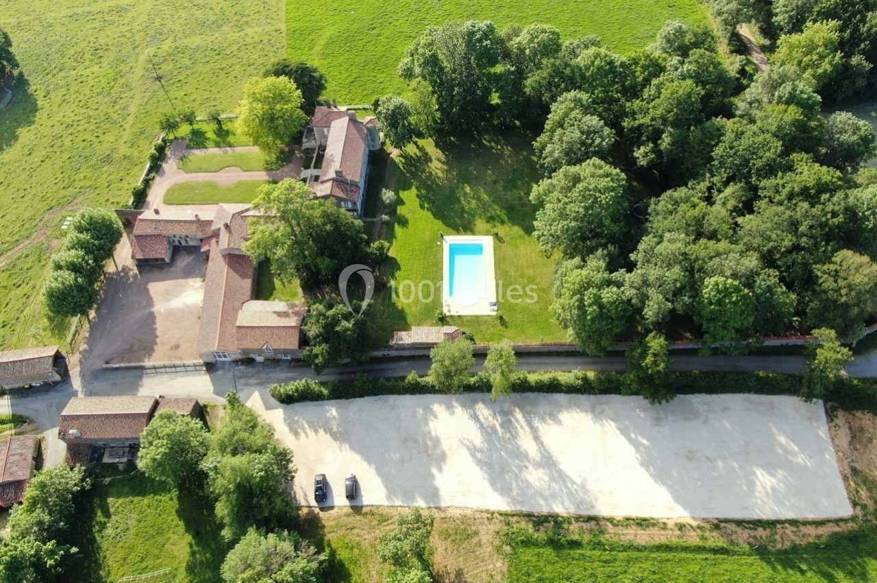 Vue aérienne d'une propriété rurale avec bâtiments, piscine, espaces verts et parking entourés de champs et d'arbres.
