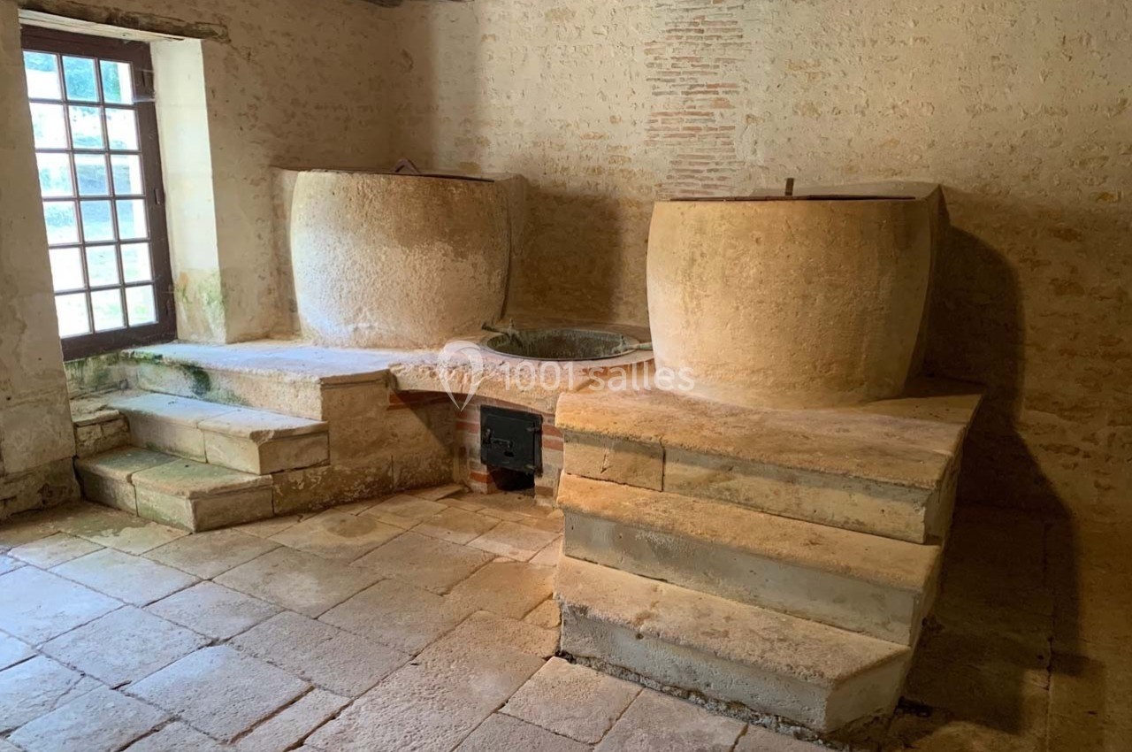 Deux cuves en pierre dans une pièce ancienne avec sol en dalles, murs en pierre et lumière naturelle d'une fenêtre.