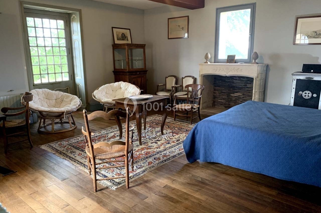 Chambre avec parquet, lit couvert d'un drap bleu, cheminée en pierre, meubles anciens et fauteuils autour d'une table.