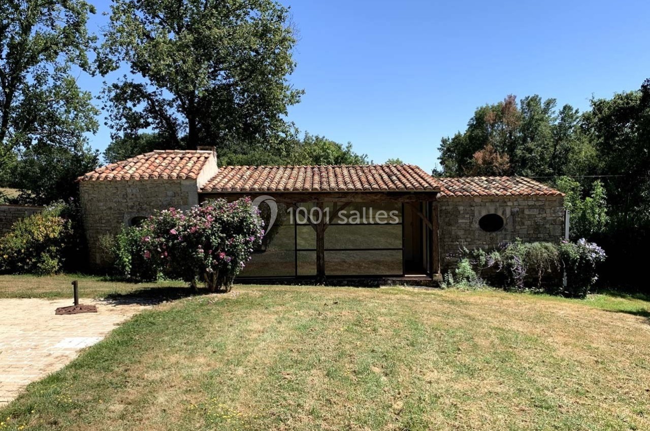 Maison en pierre avec toit en tuiles, entourée de végétation et située dans un jardin avec pelouse.