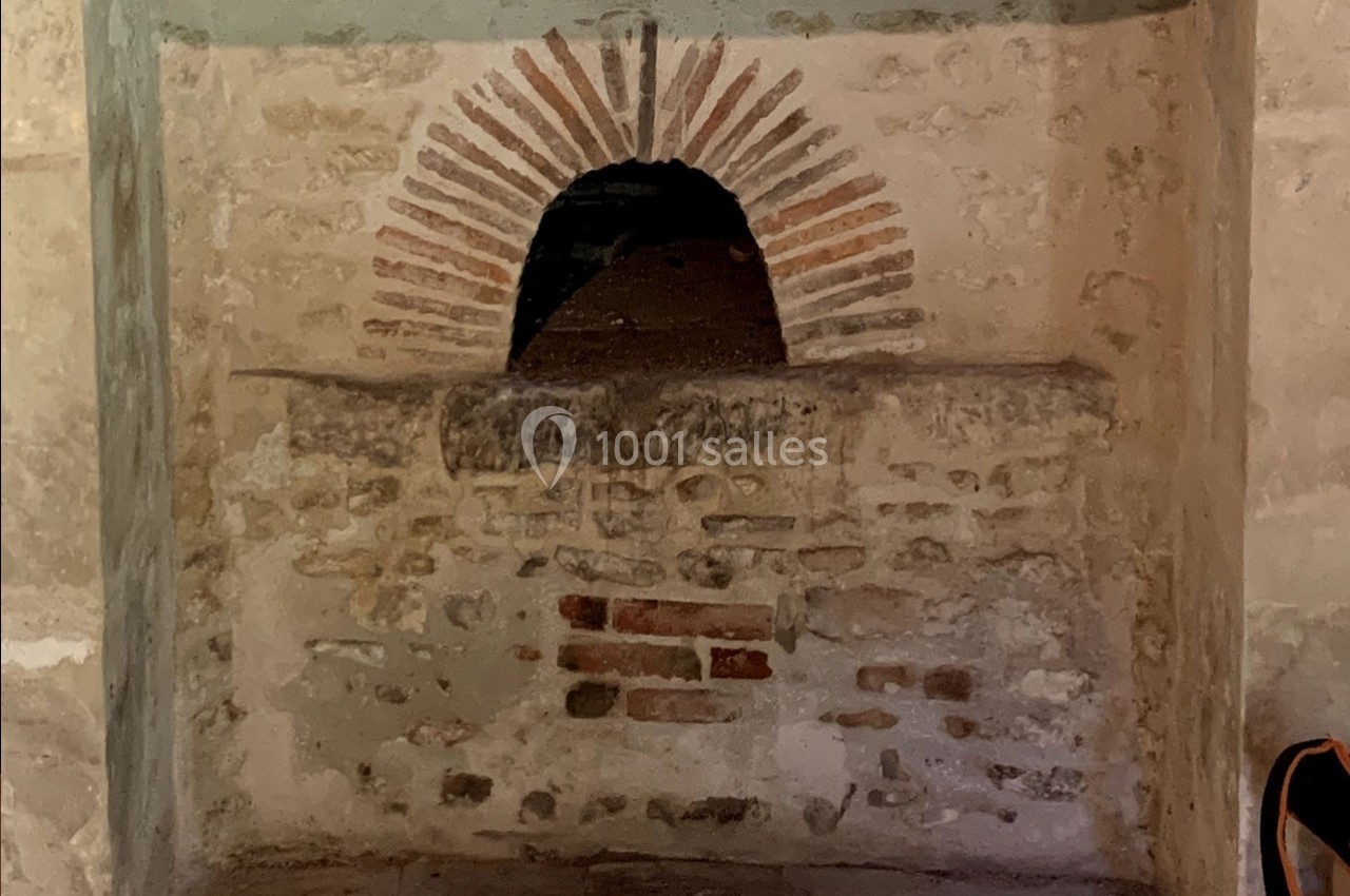 Ouverture voûtée en briques rouges dans un mur en pierre, probablement un ancien four ou une niche.