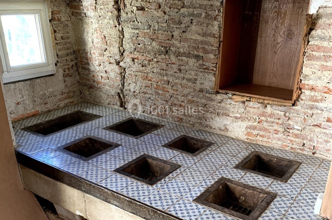 Plan de travail en carreaux décoratifs avec plusieurs ouvertures carrées, dans une pièce aux murs en briques apparentes.