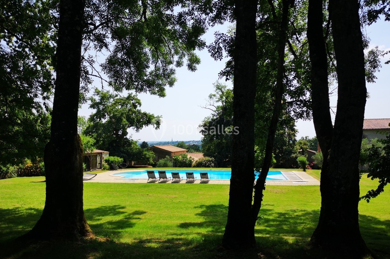 Piscine extérieure entourée de chaises longues, située dans un jardin verdoyant avec des arbres en premier plan.
