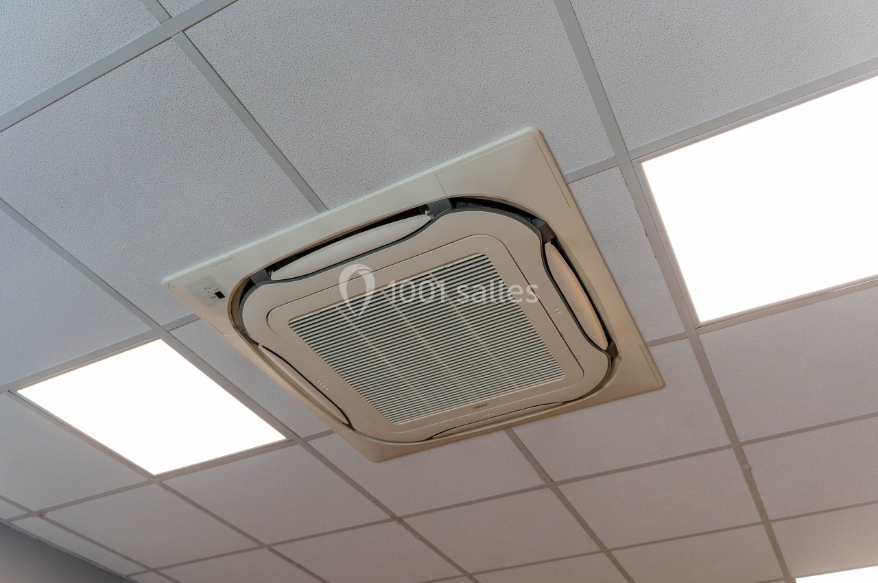 Un climatiseur encastré dans un plafond à dalles blanches, entouré de panneaux lumineux.