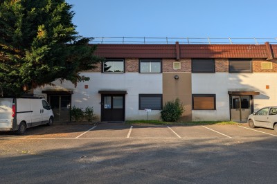 Façade d'un bâtiment commercial à deux étages avec parking et véhicules stationnés à l'avant.