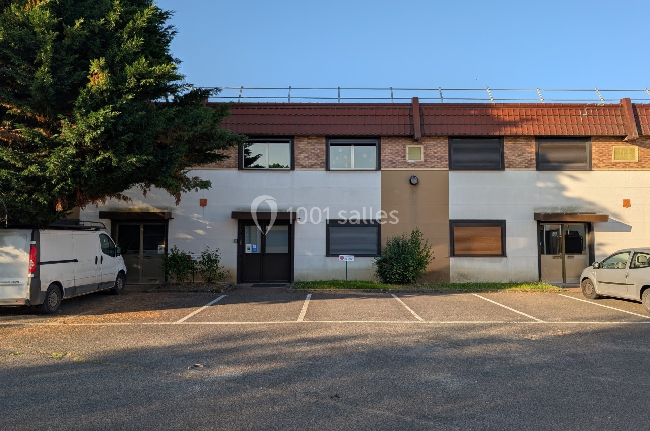 Façade d'un bâtiment commercial à deux étages avec parking et véhicules stationnés à l'avant.