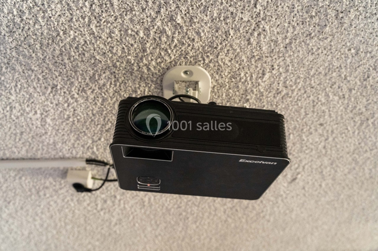 Projecteur noir fixé au plafond, orienté vers le bas, avec un câble connecté à proximité.