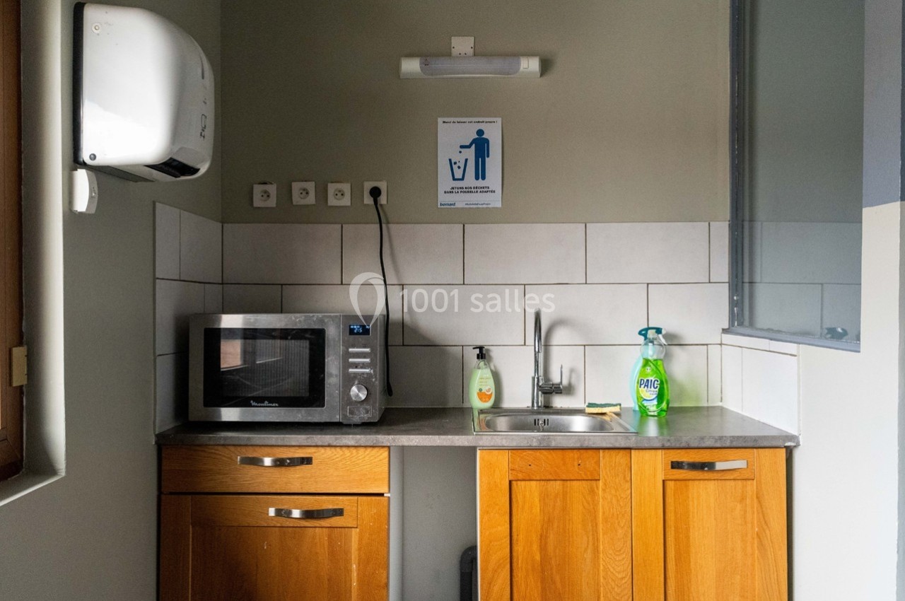 Cuisine d'appoint avec évier, micro-ondes, distributeur de savon et produit ménager sur un plan de travail.