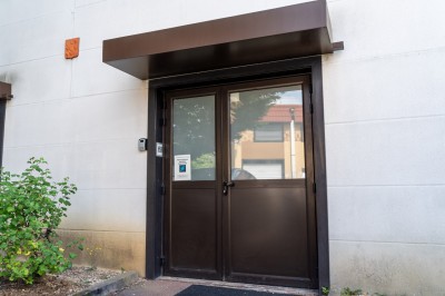 Façade d'un petit bâtiment commercial avec des places de parking et des véhicules stationnés à l'avant.