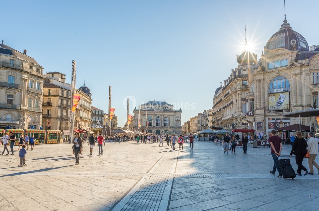 Place animée avec piétons, bâtiments historiques et soleil éclatant dans un ciel bleu clair.