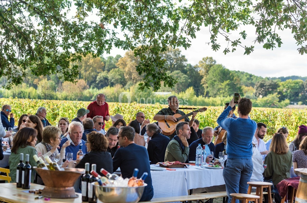 Groupe de personnes partageant un repas en plein air sous des arbres, avec un musicien jouant de la guitare.