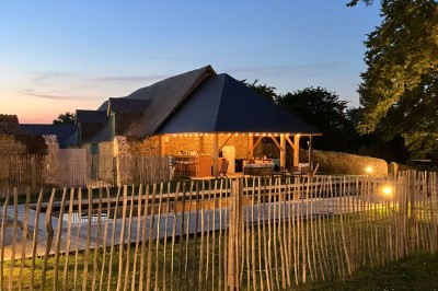 Cave voûtée en pierre avec tonneaux en bois, tabourets rustiques et escalier menant à l'extérieur.