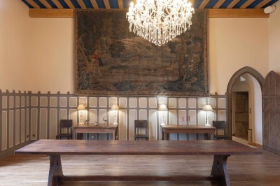 Cave voûtée en pierre avec tonneaux en bois, tabourets rustiques et escalier menant à l'extérieur.