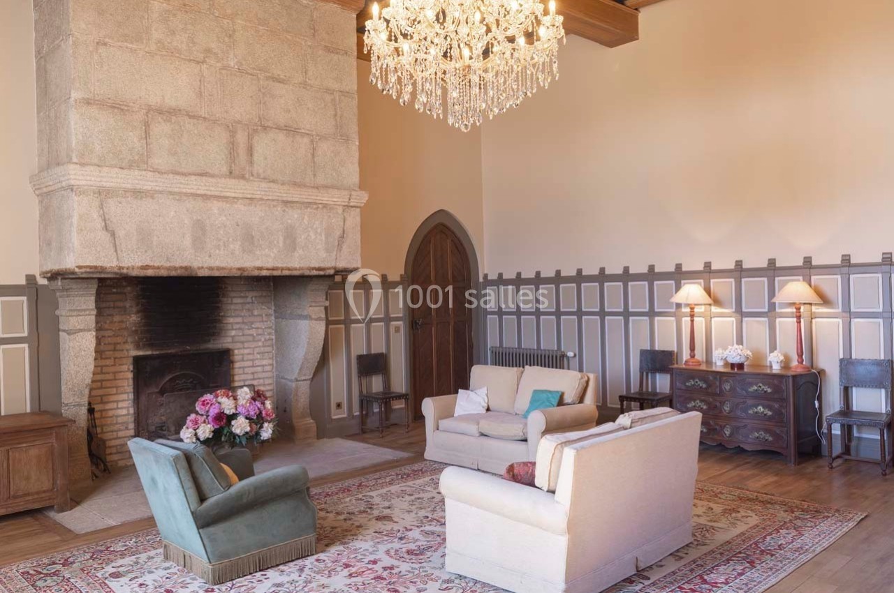 Salon élégant avec cheminée en pierre, lustre en cristal, fauteuils confortables et décoration classique.