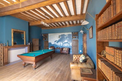 Cave voûtée en pierre avec tonneaux en bois, tabourets rustiques et escalier menant à l'extérieur.