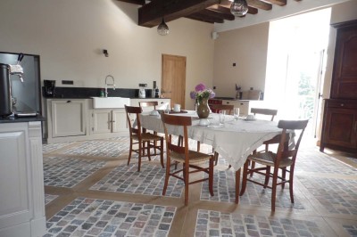 Cave voûtée en pierre avec tonneaux en bois, tabourets rustiques et escalier menant à l'extérieur.