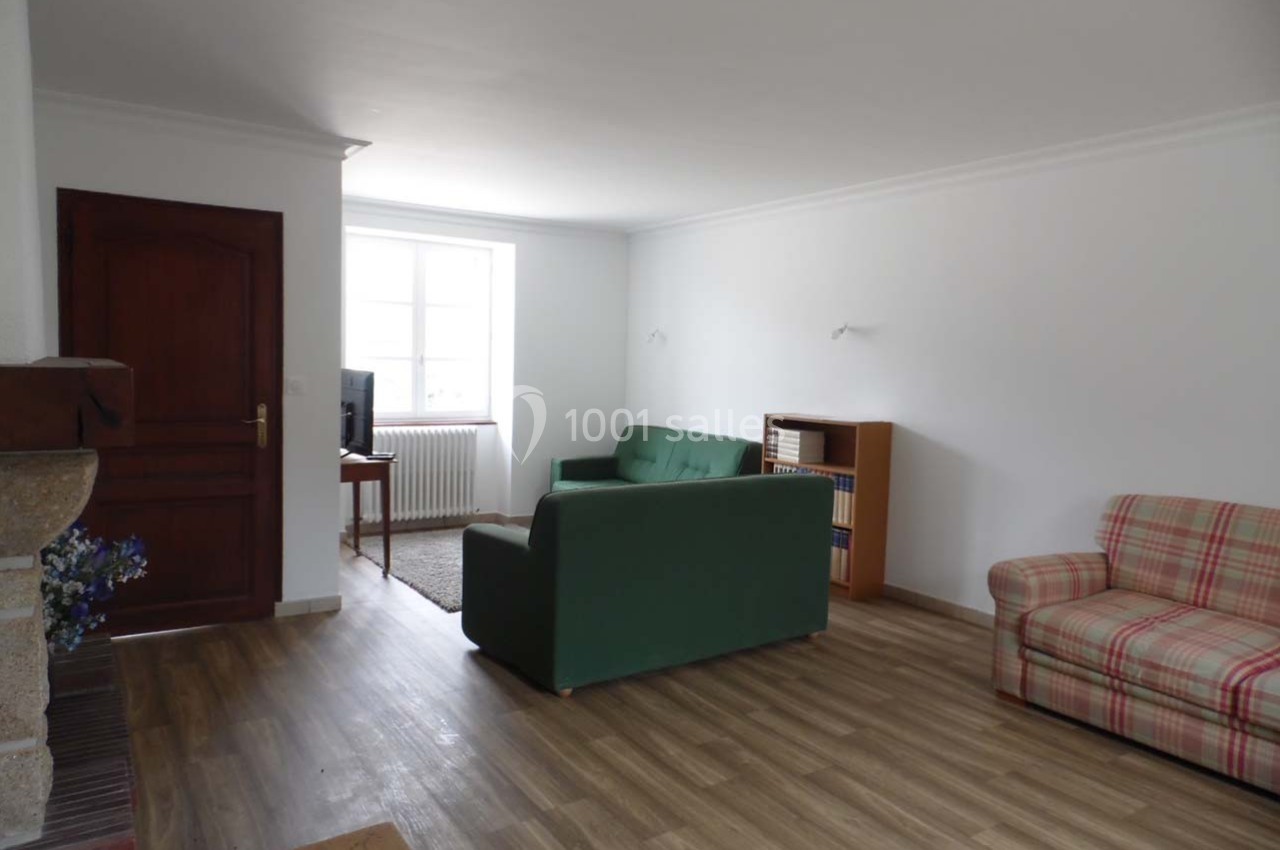 Salon lumineux avec parquet, canapé vert, fauteuil à carreaux, étagère en bois et fenêtre laissant entrer la lumière…