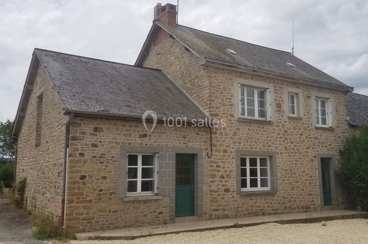 Maison en pierre avec deux étages, plusieurs fenêtres blanches et portes vertes, située dans un environnement rural.