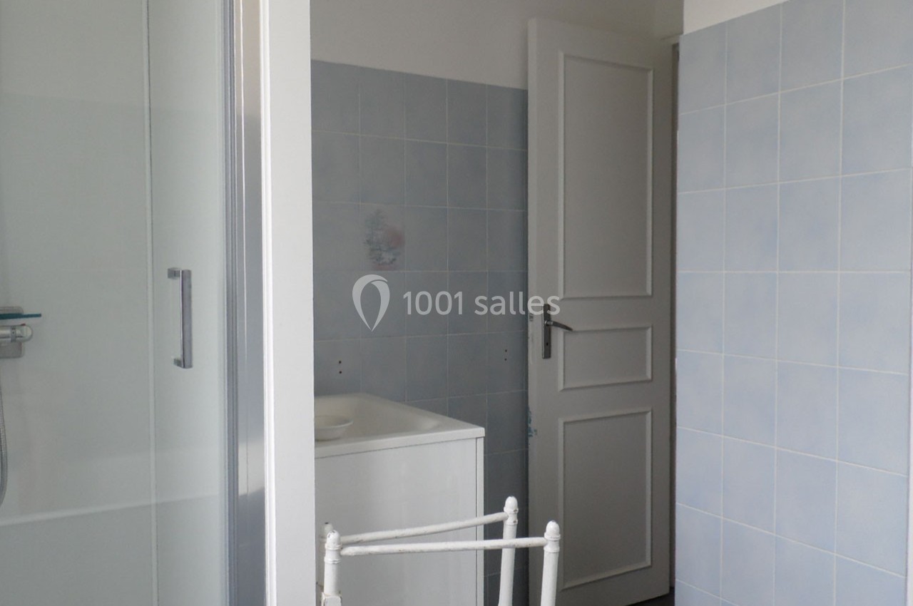Salle de bain avec murs carrelés bleus, porte blanche ouverte et cabine de douche partiellement visible.
