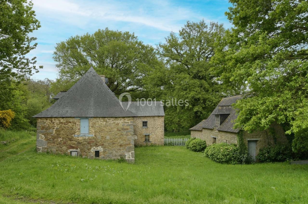 Maisons en pierre traditionnelles entourées de verdure et d'arbres sous un ciel bleu partiellement nuageux.