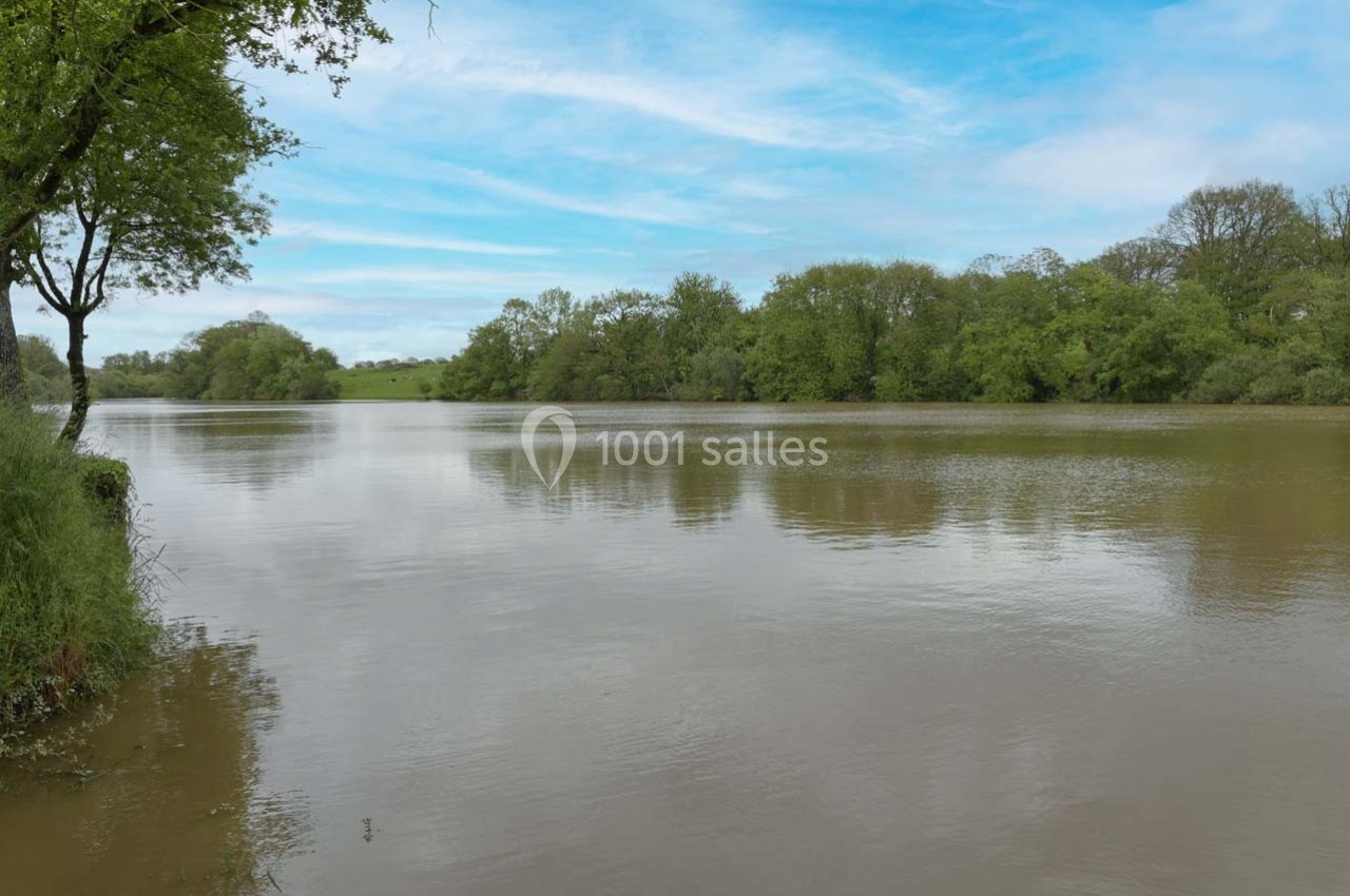 Vue d'un lac calme entouré d'arbres et de verdure sous un ciel partiellement nuageux.