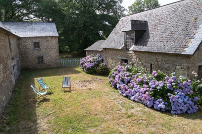Cave voûtée en pierre avec tonneaux en bois, tabourets rustiques et escalier menant à l'extérieur.