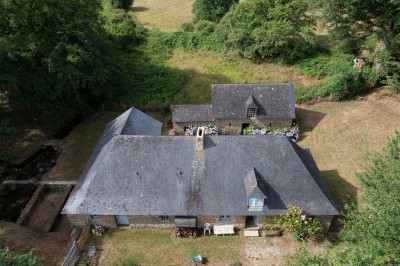 Cave voûtée en pierre avec tonneaux en bois, tabourets rustiques et escalier menant à l'extérieur.