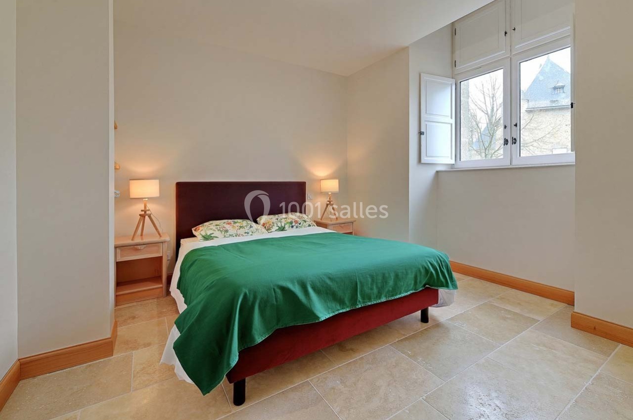 Chambre lumineuse avec un lit double, couvre-lit vert, deux lampes de chevet et une fenêtre ouverte sur l'extérieur.