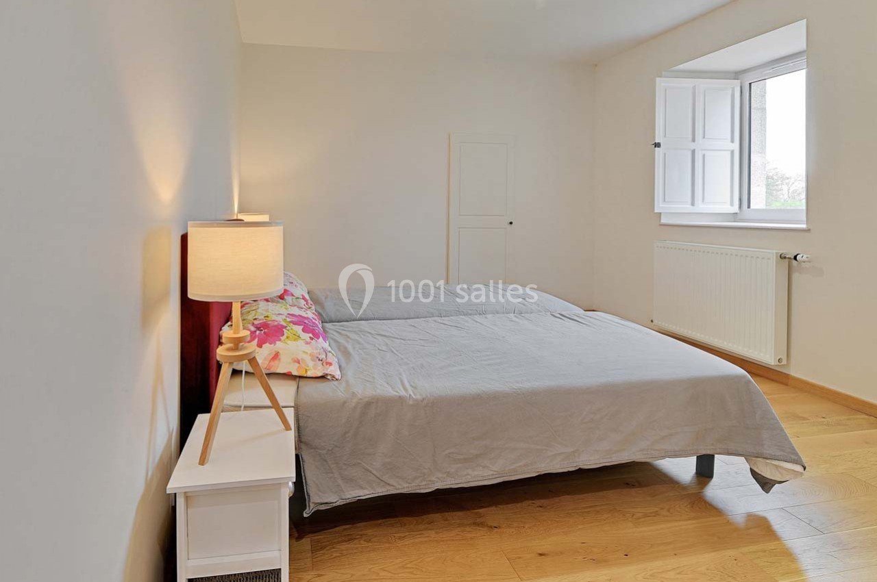 Chambre lumineuse avec deux lits simples, une lampe de chevet et un sol en parquet clair.