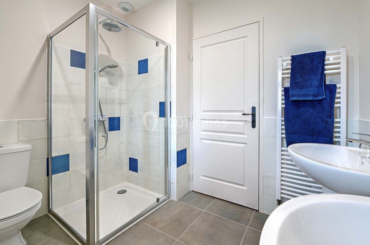 Salle de bain moderne avec douche vitrée, carrelage blanc et bleu, lavabo, toilettes et sèche-serviettes.