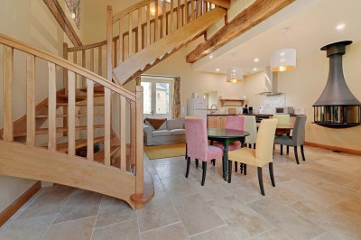 Cave voûtée en pierre avec tonneaux en bois, tabourets rustiques et escalier menant à l'extérieur.