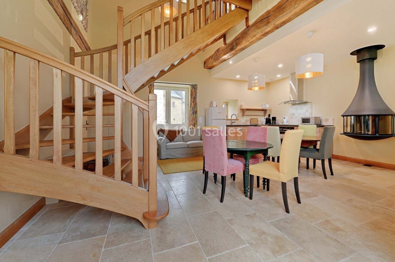 Intérieur lumineux avec escalier en bois, coin salon, table à manger colorée et cuisine ouverte moderne.
