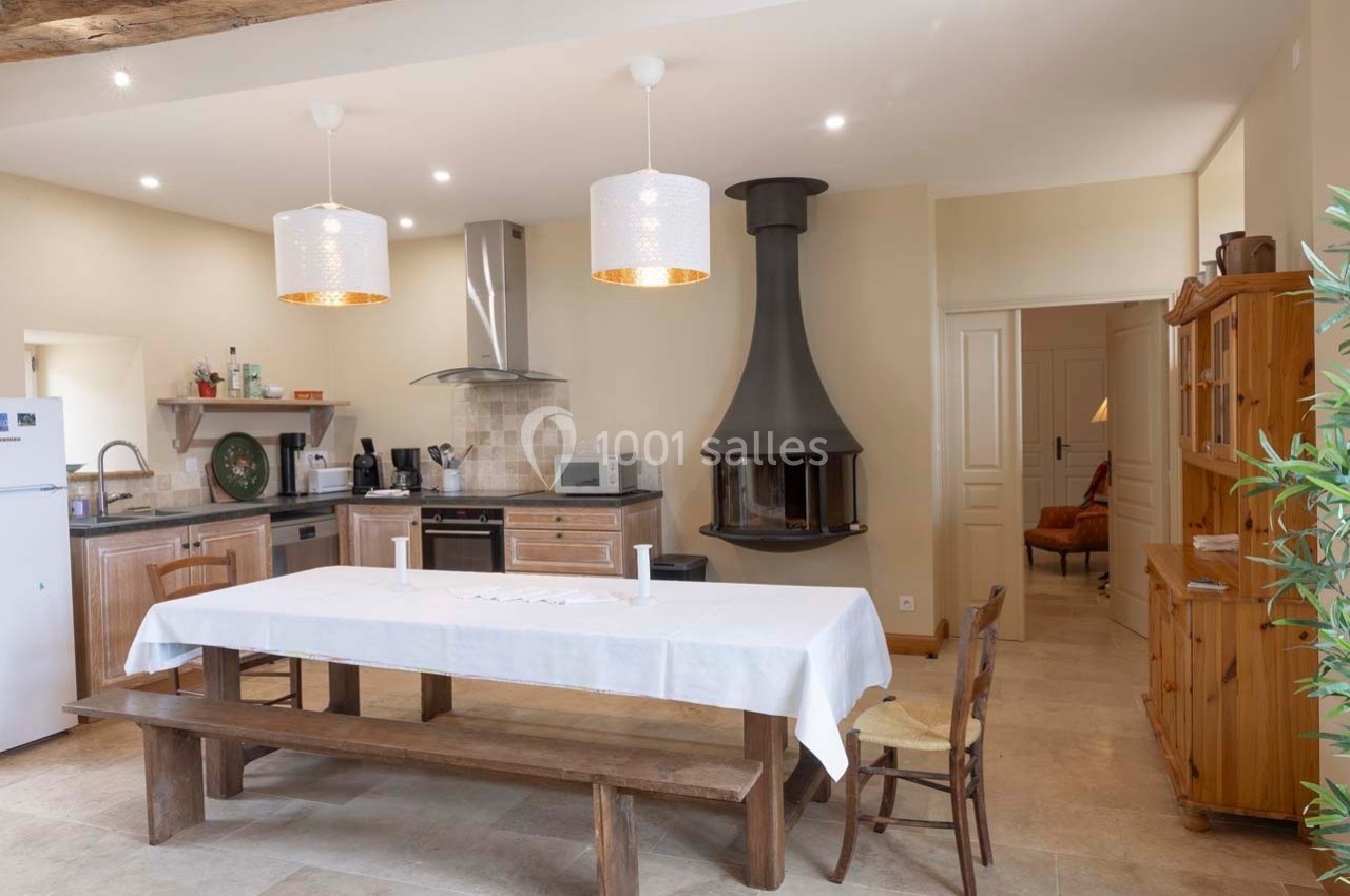 Cuisine ouverte avec table en bois, cheminée suspendue, meubles en bois et éclairage suspendu.