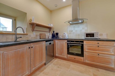 Cave voûtée en pierre avec tonneaux en bois, tabourets rustiques et escalier menant à l'extérieur.