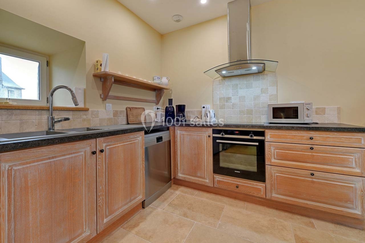 Cuisine équipée avec meubles en bois clair, plan de travail noir, électroménagers modernes et crédence en carreaux beiges.