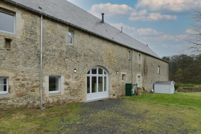 Cave voûtée en pierre avec tonneaux en bois, tabourets rustiques et escalier menant à l'extérieur.