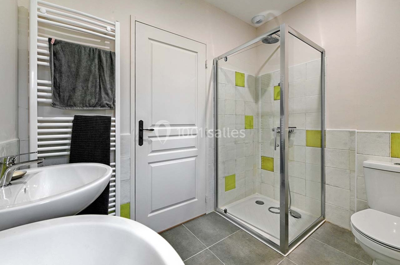 Salle de bain avec douche vitrée, lavabo double, sèche-serviettes mural et carrelage aux accents verts.