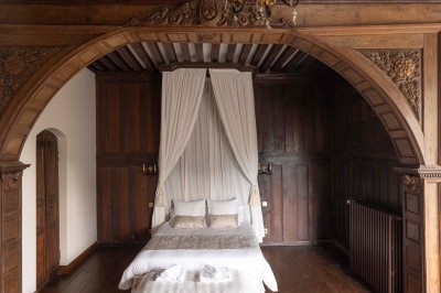 Cave voûtée en pierre avec tonneaux en bois, tabourets rustiques et escalier menant à l'extérieur.