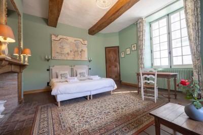 Cave voûtée en pierre avec tonneaux en bois, tabourets rustiques et escalier menant à l'extérieur.