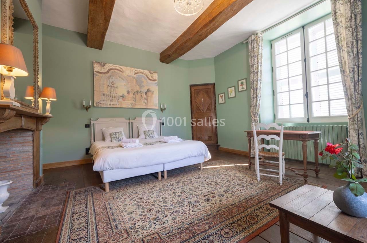 Chambre lumineuse avec lit double, poutres apparentes, murs verts, tapis coloré et mobilier en bois.