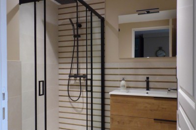 Cave voûtée en pierre avec tonneaux en bois, tabourets rustiques et escalier menant à l'extérieur.