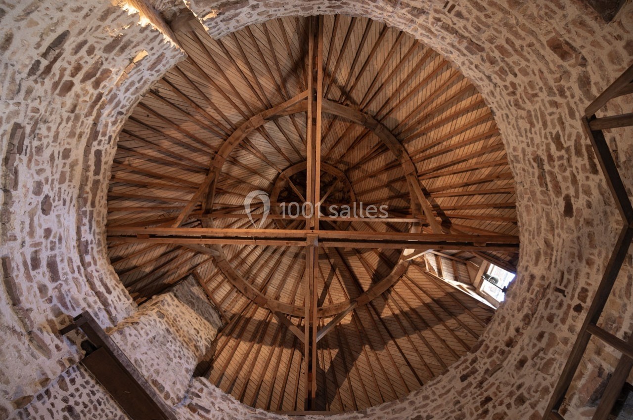 Vue intérieure d'une charpente en bois circulaire sous un toit en pierre dans un bâtiment ancien.